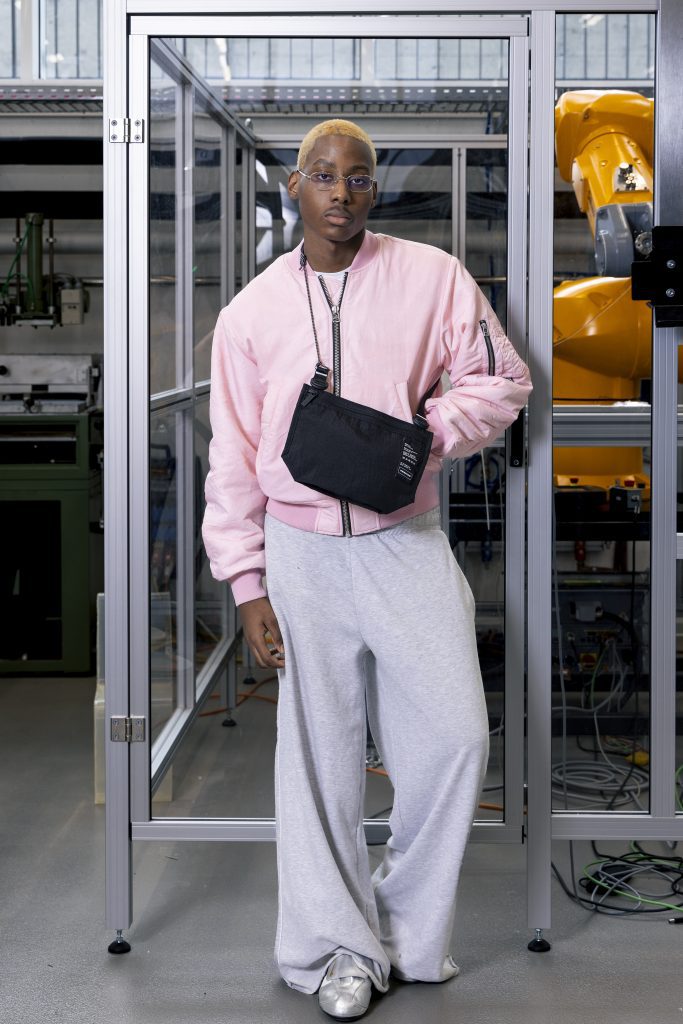 Ragazzo indossando la Mono PA6 Musette di Freitag. Indossa una felpa rosa pastello e una tuta grigia.