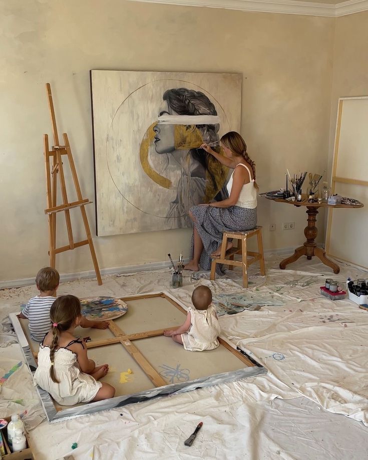 Donna dentro unastanza chiara, appositamente decorata per dipingere, che dipinge un quadro di fronte ai suoi bambini. Questo articolo parla di quanto è importante fare una cosa inutile giusto per volontà e non produttività.