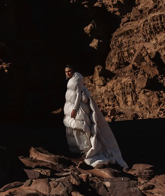 Ragazzo con un piumino colore avorio davanti a rocce arancione in un deserto