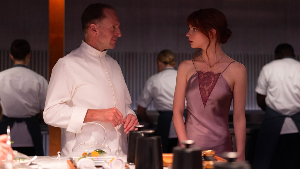 Scena del film Il Menu con lo chef Julian Slowik (Ralph Fiennes) che parla con Margot (Anya Taylor-Joy) in cucina, circondati dallo staff.