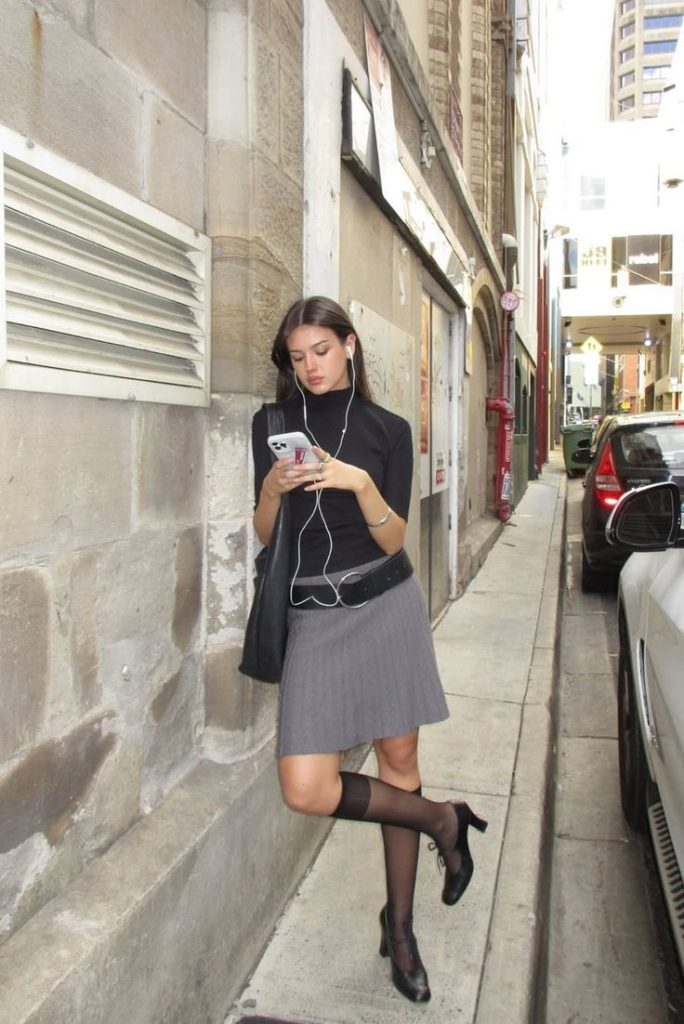 Look con una gonna midi grigia, maglietta basica nera con maniche lunghe e stivali neri alti