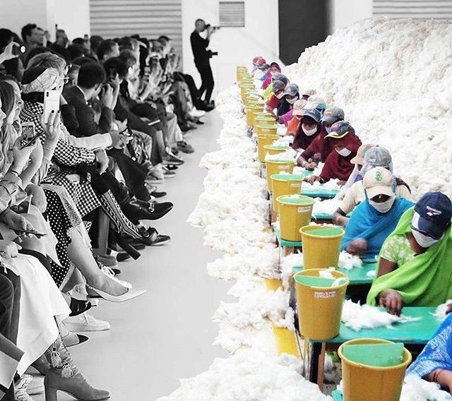 Immagina editata graficamente di una sfilata in cui si vedono persone importanti in prima fila e anziche avere modelle sfilando ci sono lavoratori a fare i capi che sfilano