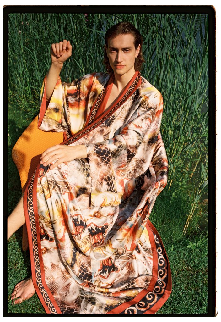 Modello indossando lz collezione SS26 di Ginny Litscher, è seduto e guarda alla camara.