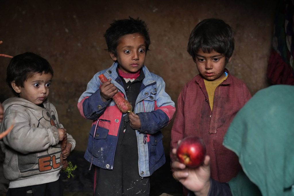 Madre afghana che porta una mela ai suoi tre bambini. I tre bambini la guardano sorpresi e scioccati della sua scoperta.