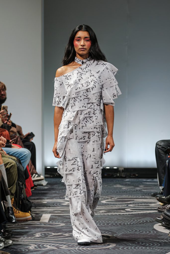 Look 29 della sfilata dello stilista APUJAN che ha sfilato il 1 settembre alla fashion week di Londra. La modella indossa un completto di maglietta asimmetrica e pantaloni fatti da pagine di crociverba in bianco e nero