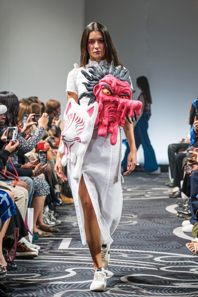 Look 3 della sfilata di APUJAN. Siccome la collezione è ispirata alla leggenda di Momotaro (Giappone) in cui il protagonista deve sconfiggere demoni, questo vestito ha due facce di demoni sul fronte del vestito, bianco e lineare.