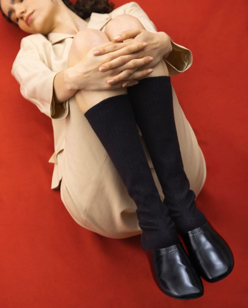 Foto editoriale del brand MICHEL PIZA. Modella che indossa il modello di stivale MAIA fatto con la tomaia in pelle nera e scaldamuscoli neri in maglia a costine