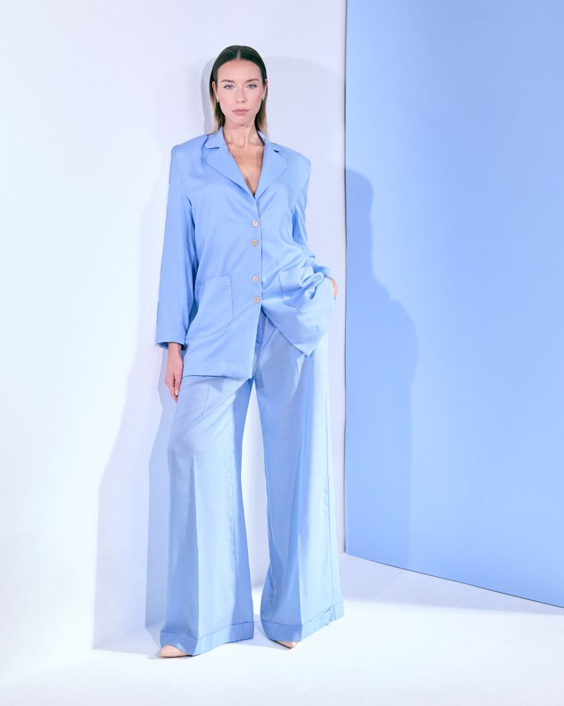 Donna in completo sartoriale azzurro polvere, giacca morbida e pantaloni ampi.
Look elegante e minimal, valorizzato da linee pulite e palette monocromatica.