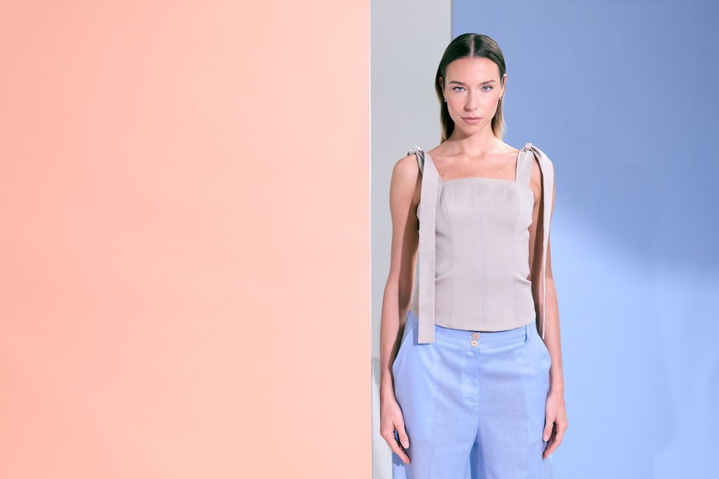 Donna con top strutturato color sabbia e pantaloni azzurro chiaro, silhouette pulita e moderna.
Estetica minimal e raffinata, giocata su contrasti delicati e geometrie cromatiche.