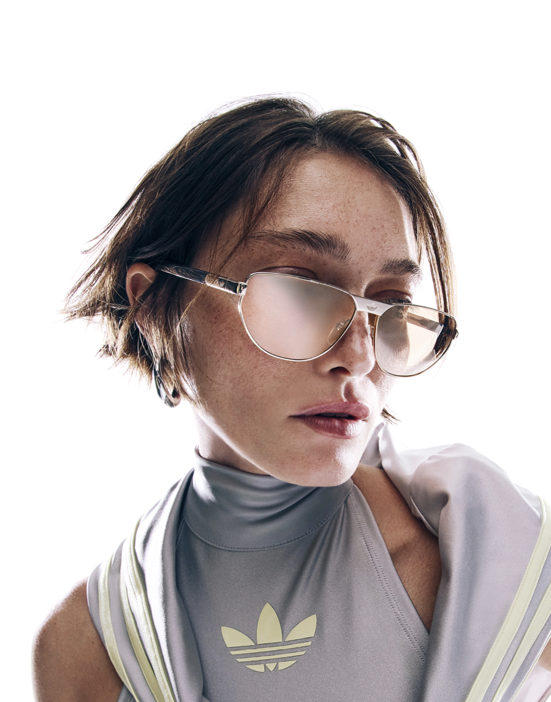 Modella che indossa occhiali da sole Adidas, su sfondo neutro.