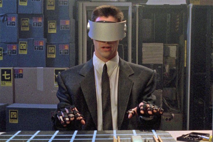 Keanu Reeves con visore tecnologico in una scena futuristica del film cyberpunk Johnny Mnemonic.

