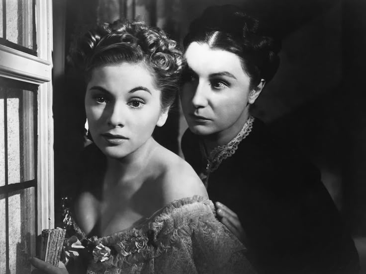 Scena in bianco e nero da Rebecca di Alfred Hitchcock, con due donne in un’atmosfera gotica e misteriosa vicino a una finestra.